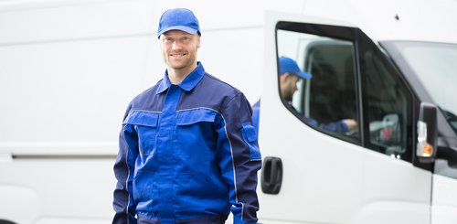 Ein Mann in Arbeitskleidung der vor einem Firmenbulli steht