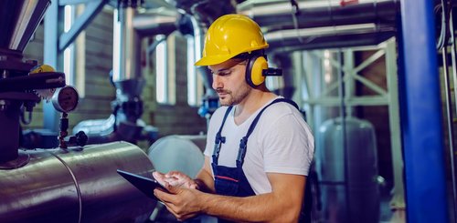 Ein Mann mit Bauhelm steht mit einem Tablet in einem Rohrraum